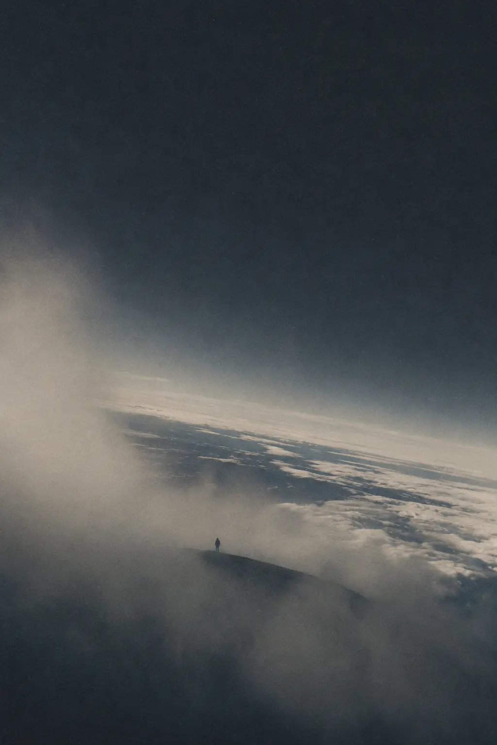 A lone figure standing above the clouds as the fog opens onto the horizon